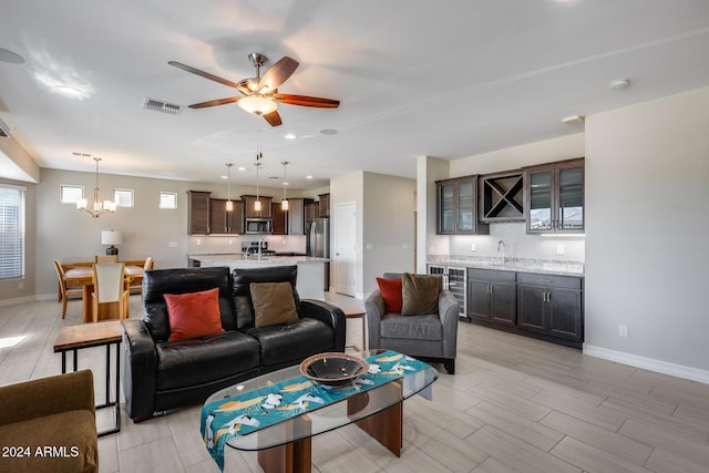 living room with ceiling fan with notable chandelier, sink, and wine cooler