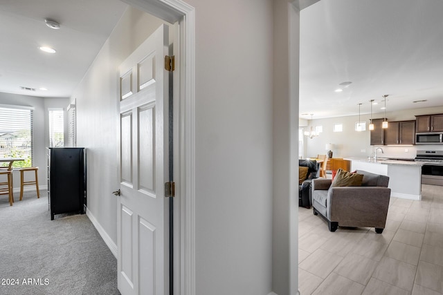 hallway featuring sink, light colored carpet, and an inviting chandelier