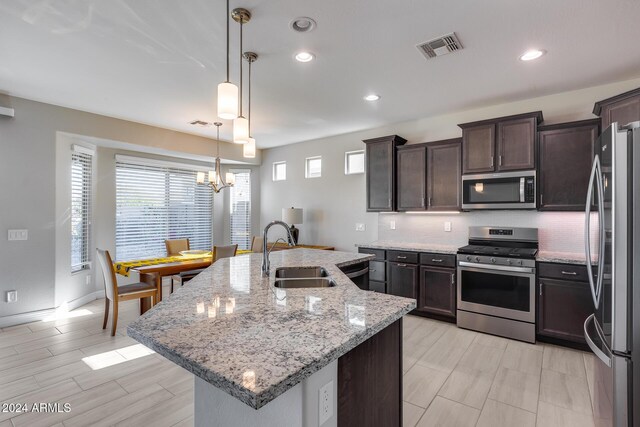 kitchen featuring a center island with sink, sink, hanging light fixtures, light stone countertops, and stainless steel appliances