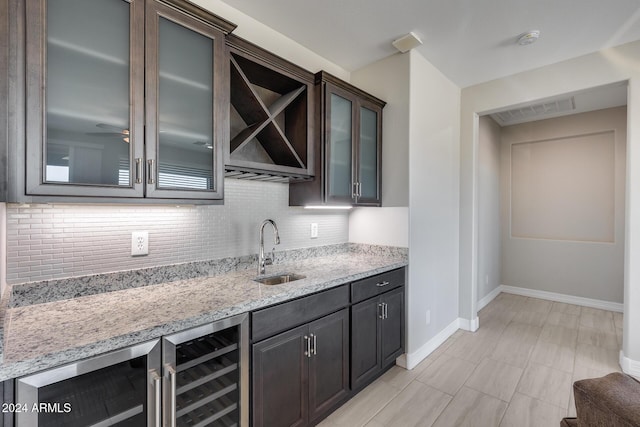 bar with wine cooler, light stone countertops, sink, and dark brown cabinets