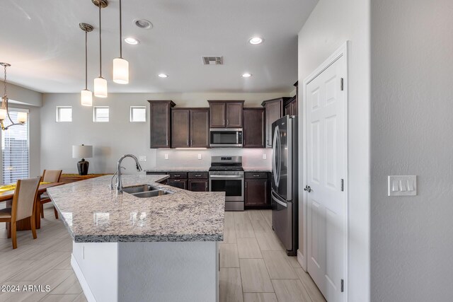 kitchen featuring dark brown cabinetry, sink, hanging light fixtures, a center island with sink, and appliances with stainless steel finishes