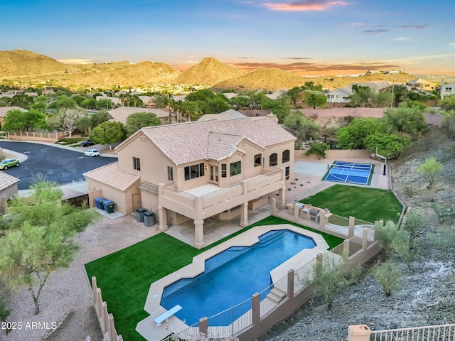 back of property at dusk with stucco siding, a lawn, a fenced backyard, a balcony, and a fenced in pool