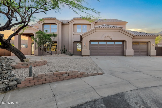 mediterranean / spanish home featuring concrete driveway, stucco siding, a tiled roof, and a garage