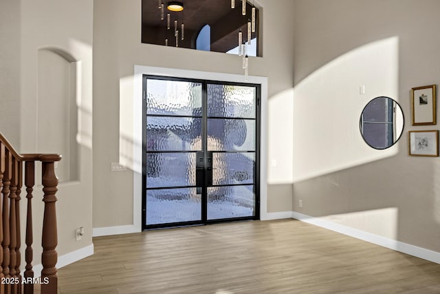 foyer with baseboards, a towering ceiling, and wood finished floors