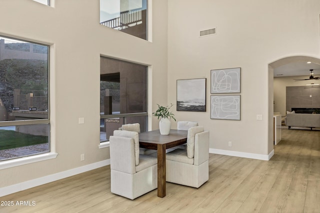 dining space featuring wood finished floors, a towering ceiling, visible vents, arched walkways, and a ceiling fan