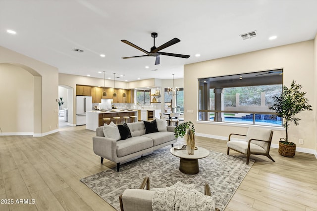 living area with a ceiling fan, baseboards, visible vents, arched walkways, and light wood-type flooring