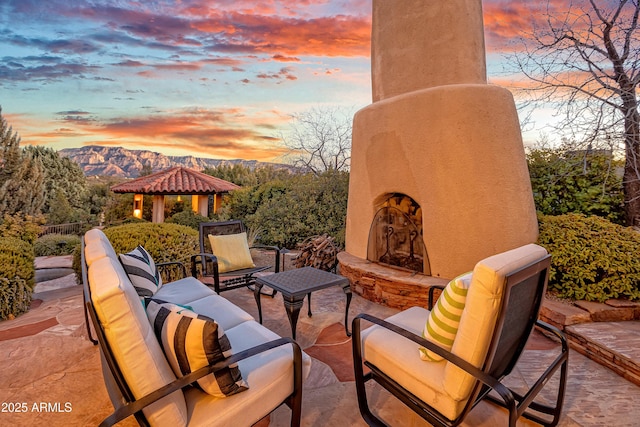 patio terrace at dusk featuring a gazebo, an outdoor living space with a fireplace, and a mountain view