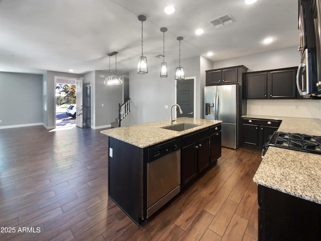 kitchen with sink, decorative light fixtures, light stone counters, an island with sink, and stainless steel appliances