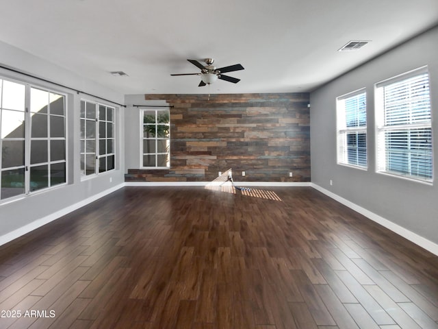 unfurnished living room with ceiling fan, dark hardwood / wood-style floors, and wooden walls