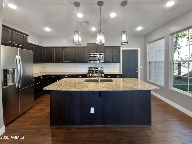 kitchen with sink, a kitchen island with sink, light stone countertops, and stainless steel appliances