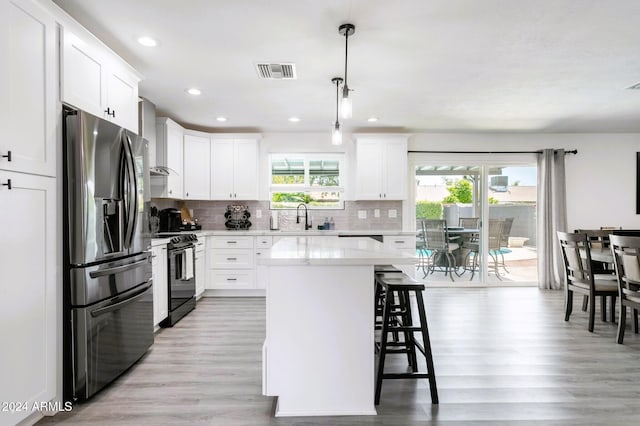 kitchen featuring a kitchen breakfast bar, electric range, stainless steel fridge, decorative light fixtures, and a kitchen island