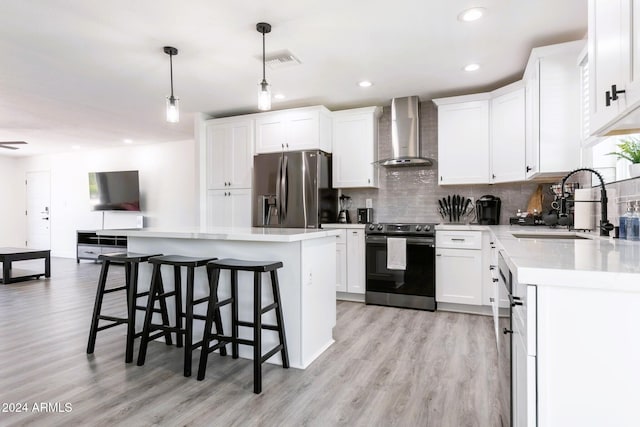 kitchen featuring white cabinetry, a center island, wall chimney range hood, pendant lighting, and appliances with stainless steel finishes