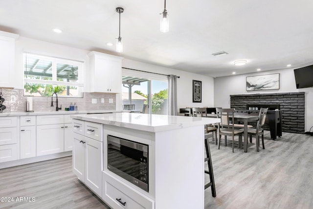 kitchen with stainless steel microwave, white cabinets, hanging light fixtures, light wood-type flooring, and a kitchen island