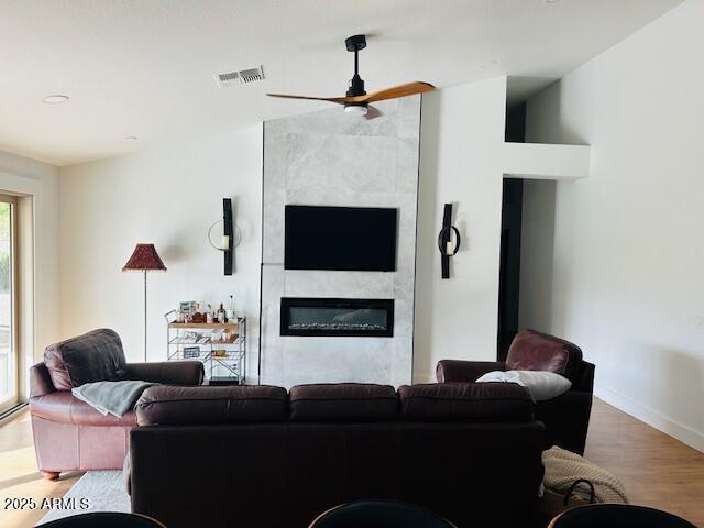 living area with a ceiling fan, a fireplace, wood finished floors, and baseboards