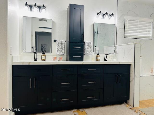 bathroom with double vanity and a marble finish shower