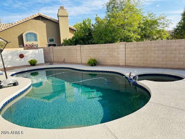 view of pool featuring a fenced backyard and a pool with connected hot tub