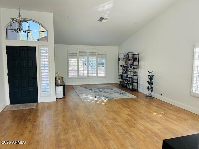 entrance foyer with a chandelier, plenty of natural light, lofted ceiling, wood finished floors, and baseboards