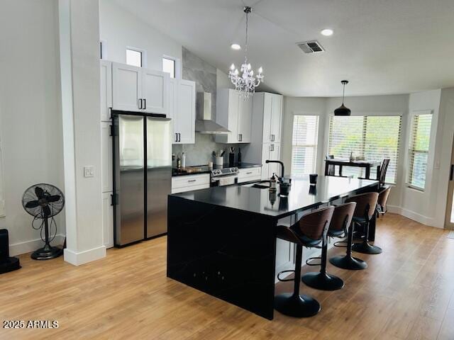 kitchen with stainless steel appliances, a sink, wall chimney range hood, dark countertops, and a kitchen breakfast bar