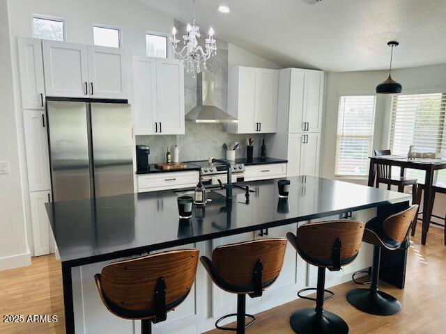 kitchen with stainless steel appliances, backsplash, dark countertops, vaulted ceiling, and an island with sink