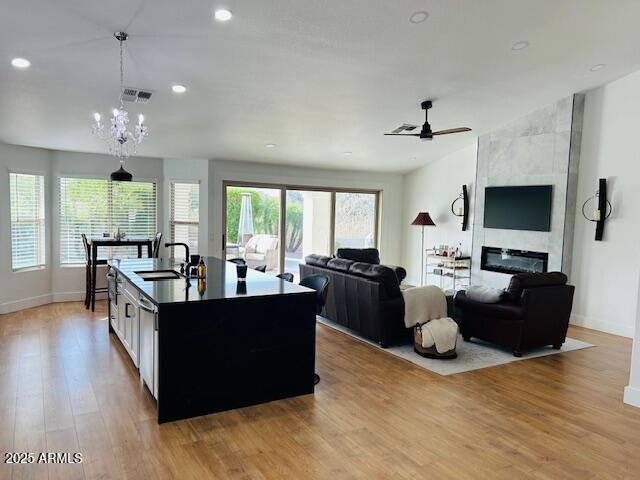 kitchen with light wood-style floors, a sink, baseboards, ceiling fan, and an island with sink