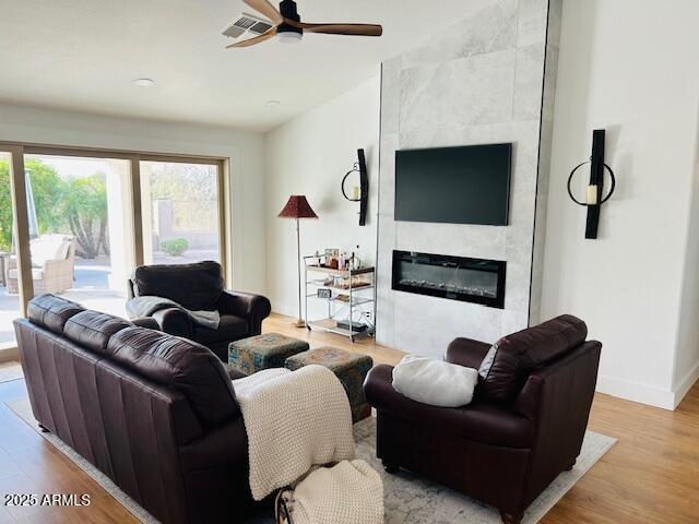 living area featuring a ceiling fan, a large fireplace, wood finished floors, and baseboards