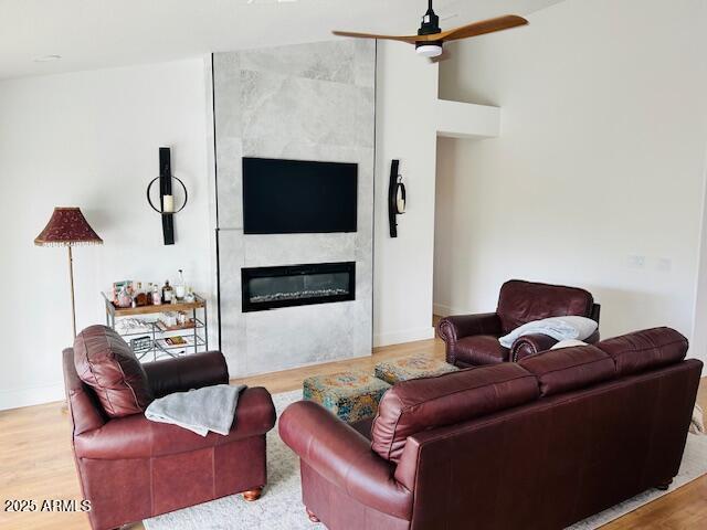 living room with a large fireplace, wood finished floors, ceiling fan, and baseboards