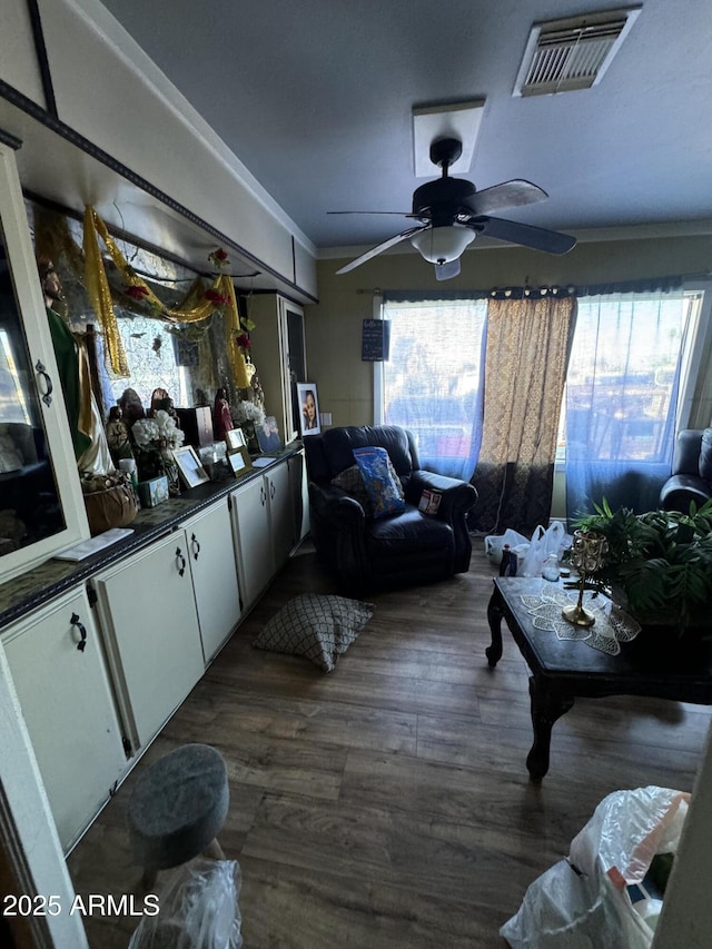 living area with a wealth of natural light, dark wood-style flooring, visible vents, and crown molding