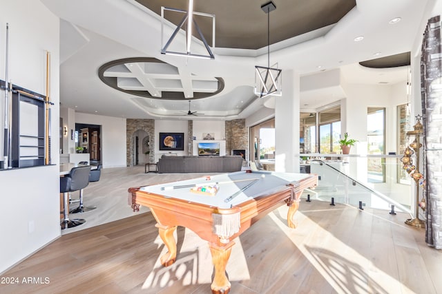 playroom with coffered ceiling, a stone fireplace, beamed ceiling, ceiling fan, and light hardwood / wood-style flooring