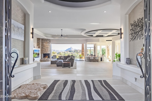 foyer featuring coffered ceiling, a fireplace, a raised ceiling, light tile patterned floors, and ceiling fan