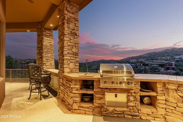 patio terrace at dusk with area for grilling, a mountain view, and a grill