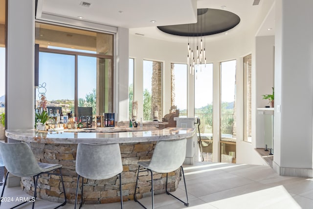 bar with an inviting chandelier, a tray ceiling, and light tile patterned floors