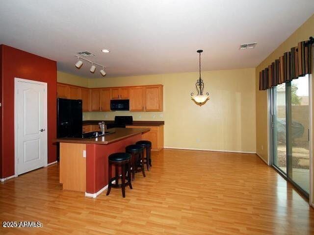 kitchen featuring a breakfast bar area, hanging light fixtures, a center island with sink, light hardwood / wood-style floors, and black appliances