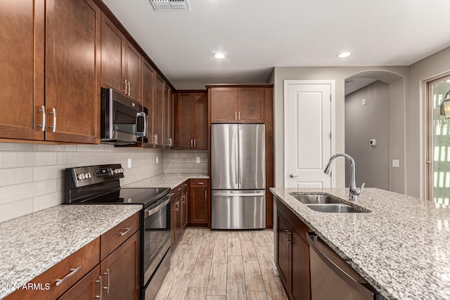 kitchen with sink, stainless steel appliances, light stone counters, light hardwood / wood-style floors, and decorative backsplash