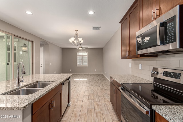 kitchen with stainless steel appliances, a kitchen island with sink, sink, an inviting chandelier, and light hardwood / wood-style floors