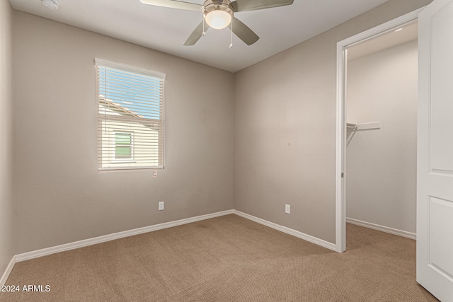 unfurnished bedroom featuring a walk in closet, ceiling fan, a closet, and light carpet