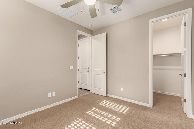 unfurnished bedroom with a walk in closet, a closet, ceiling fan, and light colored carpet