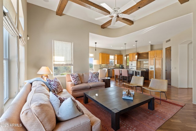 living area with a ceiling fan, visible vents, beam ceiling, and wood finished floors