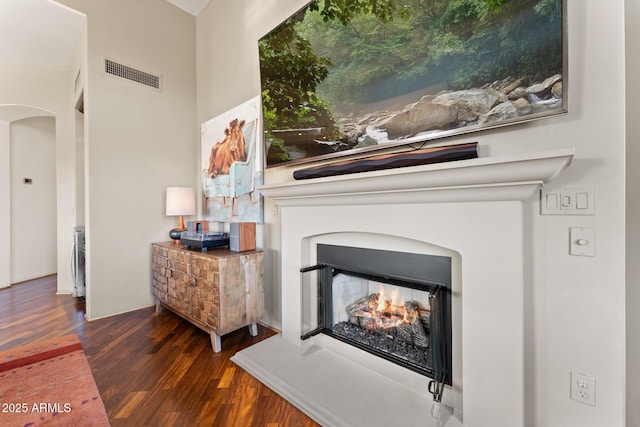 interior details featuring arched walkways, a warm lit fireplace, visible vents, and wood finished floors