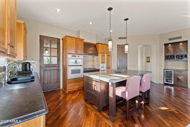 kitchen with arched walkways, white double oven, beverage cooler, a sink, and visible vents