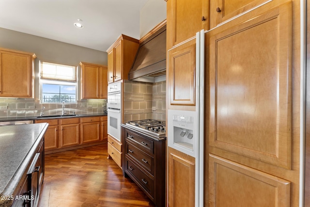 kitchen featuring dark wood-type flooring, a sink, custom exhaust hood, decorative backsplash, and stainless steel gas stovetop