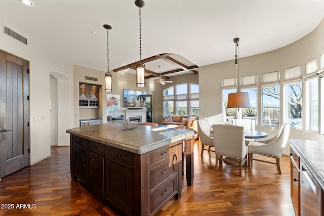 kitchen with arched walkways, a fireplace, dark wood finished floors, and pendant lighting