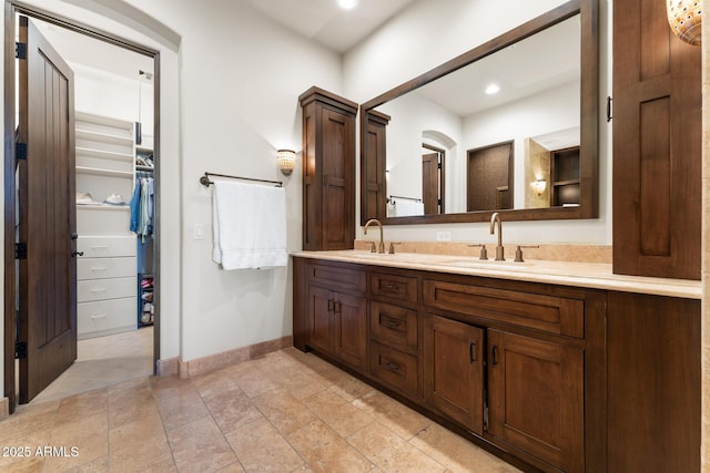 bathroom with double vanity, a sink, a walk in closet, and baseboards