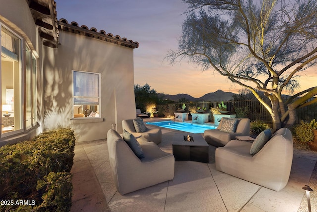 pool at dusk with a patio, a mountain view, fence, an outdoor living space, and a fenced in pool