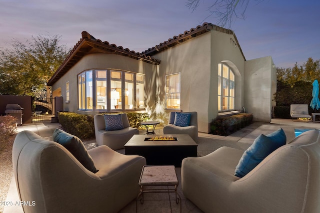 back of property at dusk featuring stucco siding, a patio area, an outdoor living space with a fire pit, and a gate