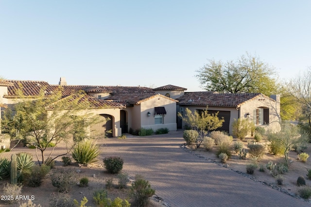 mediterranean / spanish house featuring decorative driveway, an attached garage, a tile roof, and stucco siding