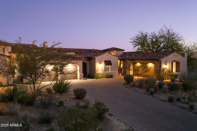 mediterranean / spanish-style house featuring decorative driveway, an attached garage, a tile roof, and stucco siding