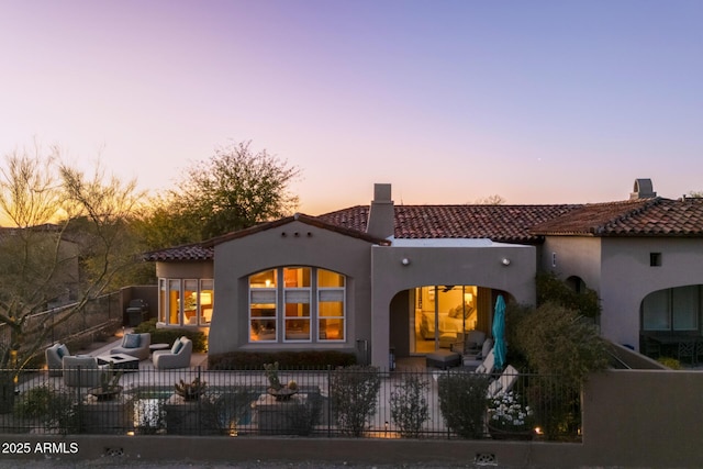 back of house at dusk featuring a tile roof, stucco siding, outdoor lounge area, a patio area, and fence private yard