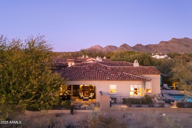 back of property at dusk with a patio area, a tile roof, a mountain view, and stucco siding