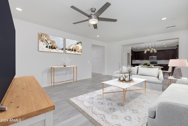 living room with ceiling fan with notable chandelier and light hardwood / wood-style floors