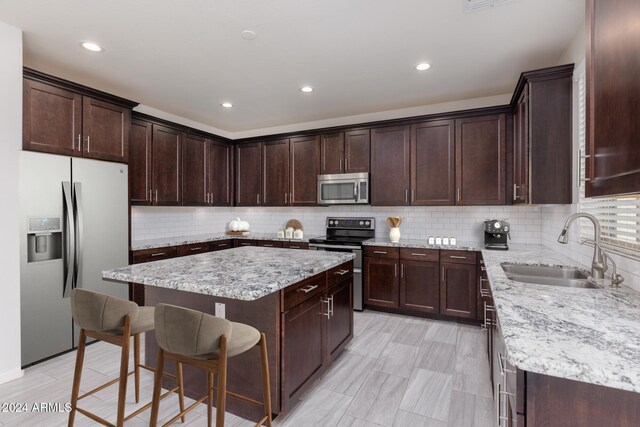 kitchen featuring ceiling fan, appliances with stainless steel finishes, tasteful backsplash, a kitchen island, and light stone counters